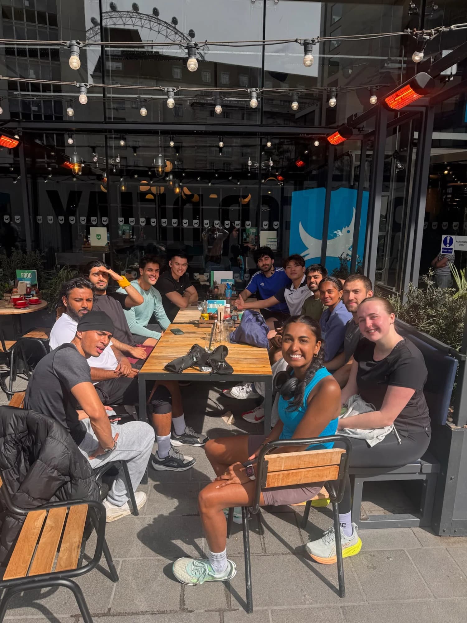 A group chatting around a long table on a sunny café terrace