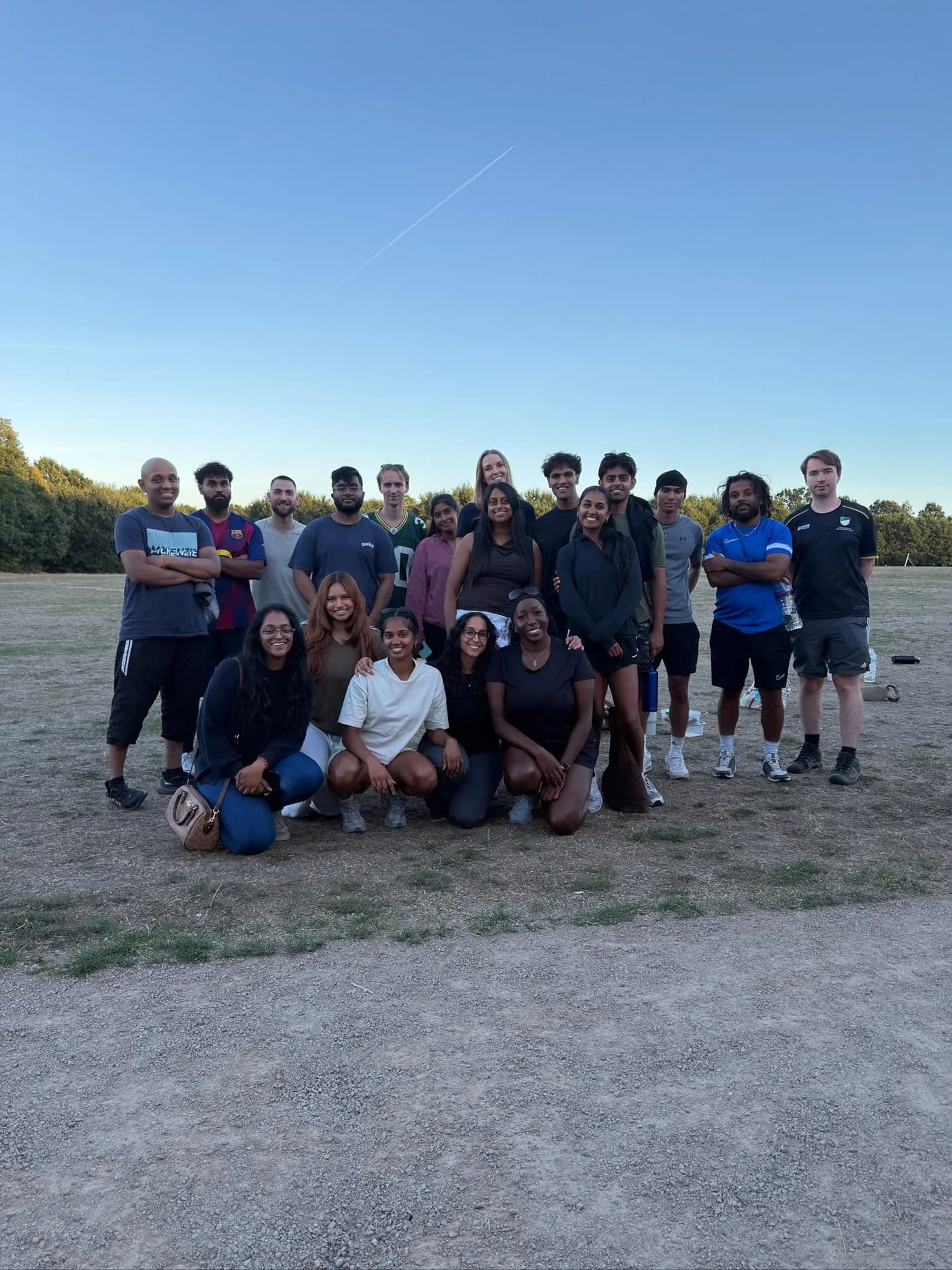 A large group posing together in an open field under a clear evening sky