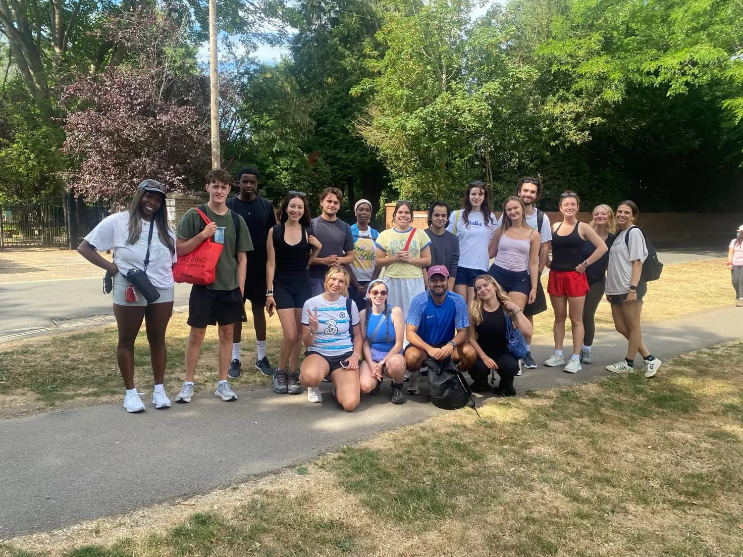 A big group smiling together on a sunny path beside tall trees