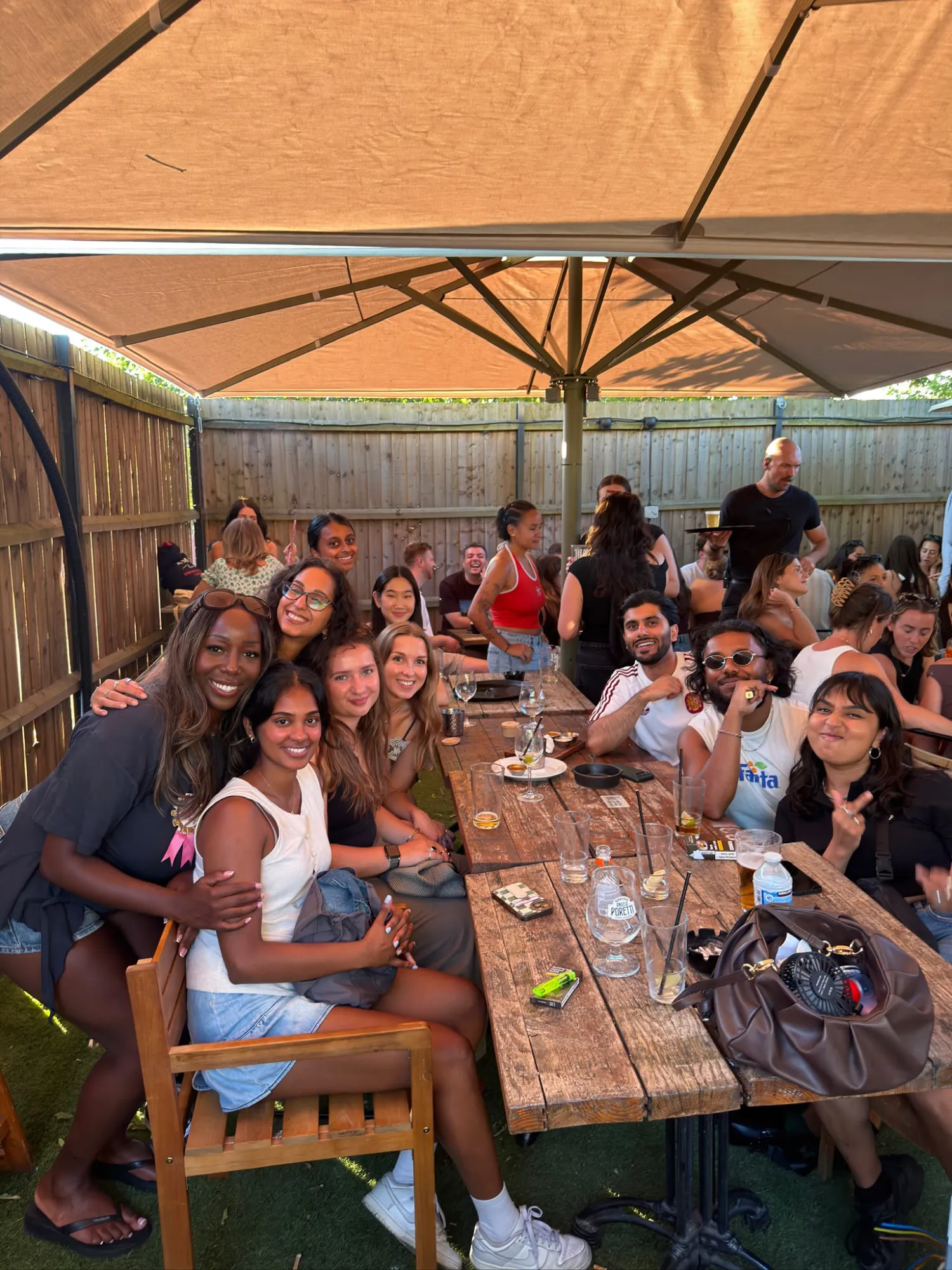 Friends gathered around a wooden table under a large garden umbrella